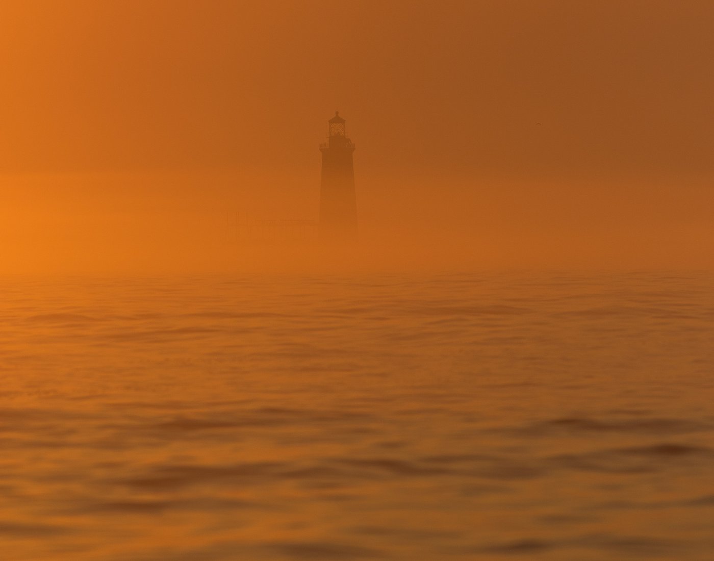 A lighthouse seen through an orange fog of sunrise.